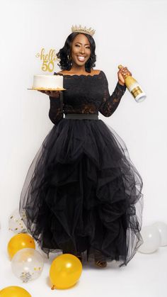 a woman in a black dress is holding a cake and some yellow balloons on the floor