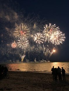 fireworks are lit up in the night sky over water and people standing on the beach