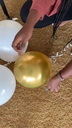 a woman is holding two balloons on the floor while another person places them in front of her