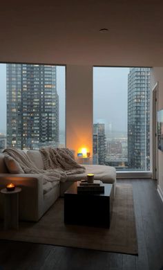 a living room filled with furniture and large windows overlooking the city at night in the evening