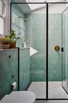 a bathroom with green tiles and a white toilet next to a walk - in shower