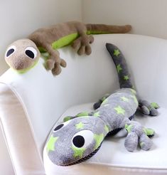 two stuffed geckos are sitting on a white chair and one is laying down