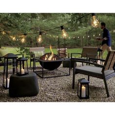 an outdoor fire pit surrounded by patio furniture and string lights with a man in the background