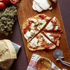 sliced pizza sitting on top of a wooden cutting board next to cheese and other foods