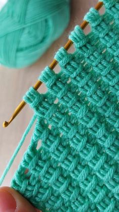 someone is stitching the stitches on their green crochet blanket with two knitting needles