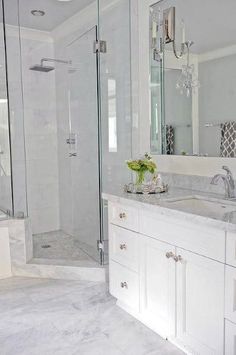 a white bathroom with marble counter tops and double sinks, shower stall and glass doors