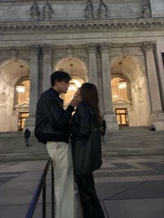 a man and woman standing in front of a large building with columns on each side