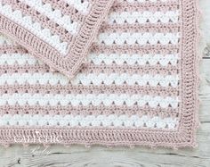 a pink and white crocheted blanket sitting on top of a wooden floor