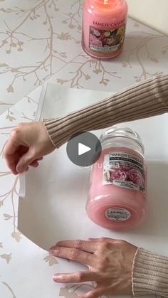 two hands are holding a jar of pink candles and another hand is reaching for it