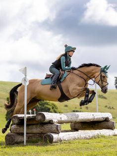 a woman riding on the back of a brown horse jumping over a wooden log obstacle