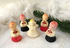 five small figurines are sitting next to a pine branch on a white cloth