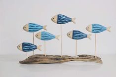 five wooden fish on sticks sitting on top of a piece of driftwood with blue and white stripes