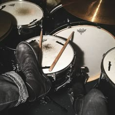 a person sitting in front of drums with their feet propped up on the drum sticks