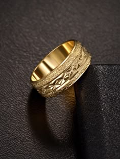 a gold wedding ring sitting on top of a black leather surface with an intricate design