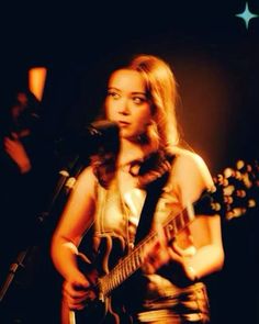 a woman holding a guitar while standing in front of a microphone