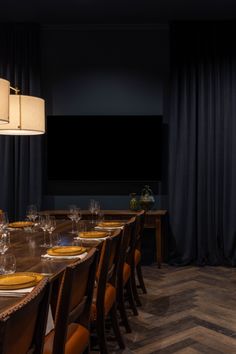 a long table set with place settings and wine glasses in front of a flat screen tv