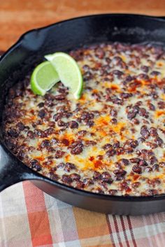 a black skillet filled with food on top of a checkered table cloth next to a lime wedge