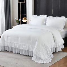 a bed with white ruffled sheets and pillows