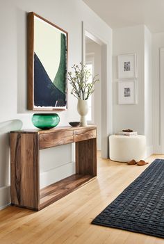 a wooden table with a vase on top of it next to a mirror and rug