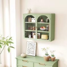 a green cabinet sitting in the corner of a living room next to a potted plant