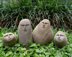 three stone faces sitting on top of green grass next to plants and bushes in the background