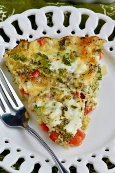 a slice of quiche with broccoli and tomatoes on a white plate next to a fork