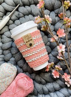 a cup of coffee sitting on top of a pile of rocks next to flowers and yarn