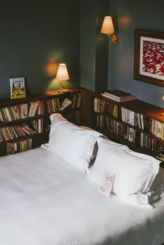 a bed with white sheets and pillows in front of bookshelves filled with dvds