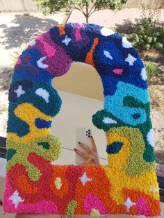 a person holding up a cell phone in front of a colorful wreath