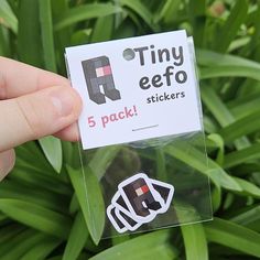 someone holding up a tiny effo sticker in front of some green plants