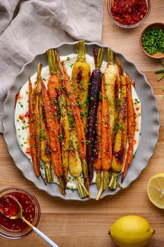 a plate full of carrots and other vegetables on a wooden table with sauces