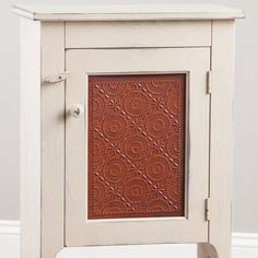 a small wooden cabinet with an ornate design on the front and sides, sitting against a white wall