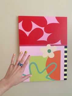 a woman's hand on top of a piece of art that is hanging on the wall