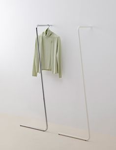 a green shirt is hanging on the wall next to a white coat rack and clothes hanger