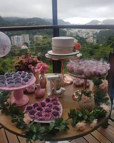 a table topped with cakes and cupcakes on top of a wooden table next to a window