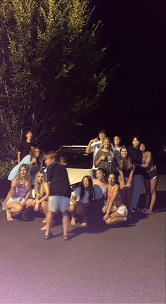 a group of people sitting on the ground in front of a car