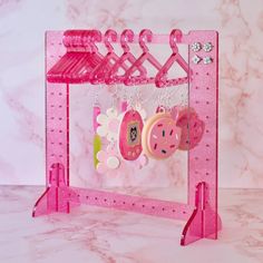 a pink jewelry rack with earrings and necklaces hanging from it's sides on a marble surface