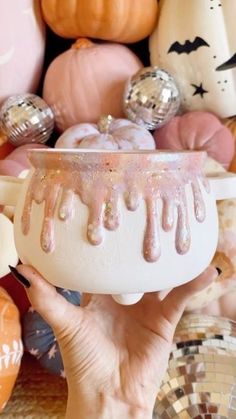 a person holding a white bowl with pink icing on it in front of pumpkins and other decorations