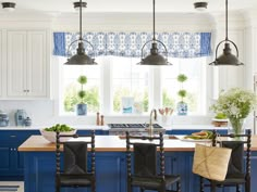 a kitchen with blue and white cabinets, an island in the center and two hanging lights above it