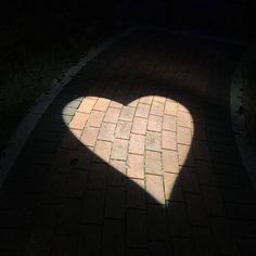 the shadow of a heart shaped object on a brick path at night with light coming through it