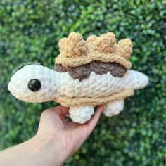 a hand holding a small crocheted stuffed animal that looks like a turtle with a crown on it's head