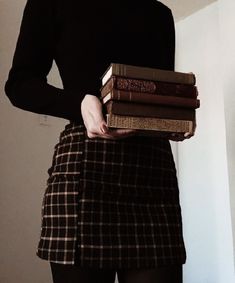 a woman is holding three books in her hands while wearing a black shirt and plaid skirt