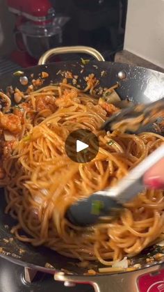 someone using tongs to stir spaghetti in a wok