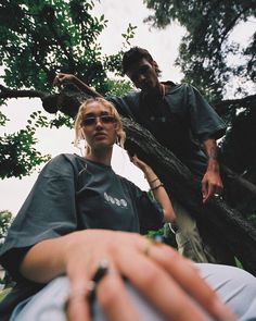 a man and woman standing next to each other in front of a tree with their hands on the ground