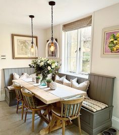 a dining room table and bench with flowers in vases on the top, sitting next to two windows