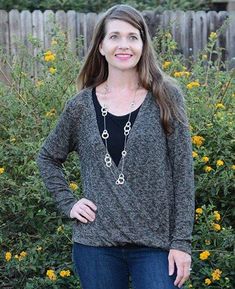 a woman is standing in front of some bushes and flowers wearing a black top with blue jeans