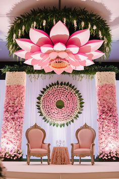 an elaborately decorated stage with two chairs and a large pink flower on the wall