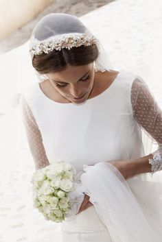 a woman in a white dress holding a bouquet and wearing a veil with flowers on it