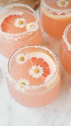 four glasses filled with pink liquid and garnished with white flowers on the rims