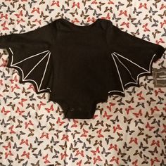 a black bodysuit with white bat wings on it's chest, laying on a bed